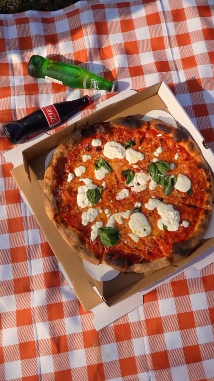 Casano's Round whole pie on a wooden peel — leoparded crust, red-sauce sheen, mozzarella pull at the center, scattered basil.