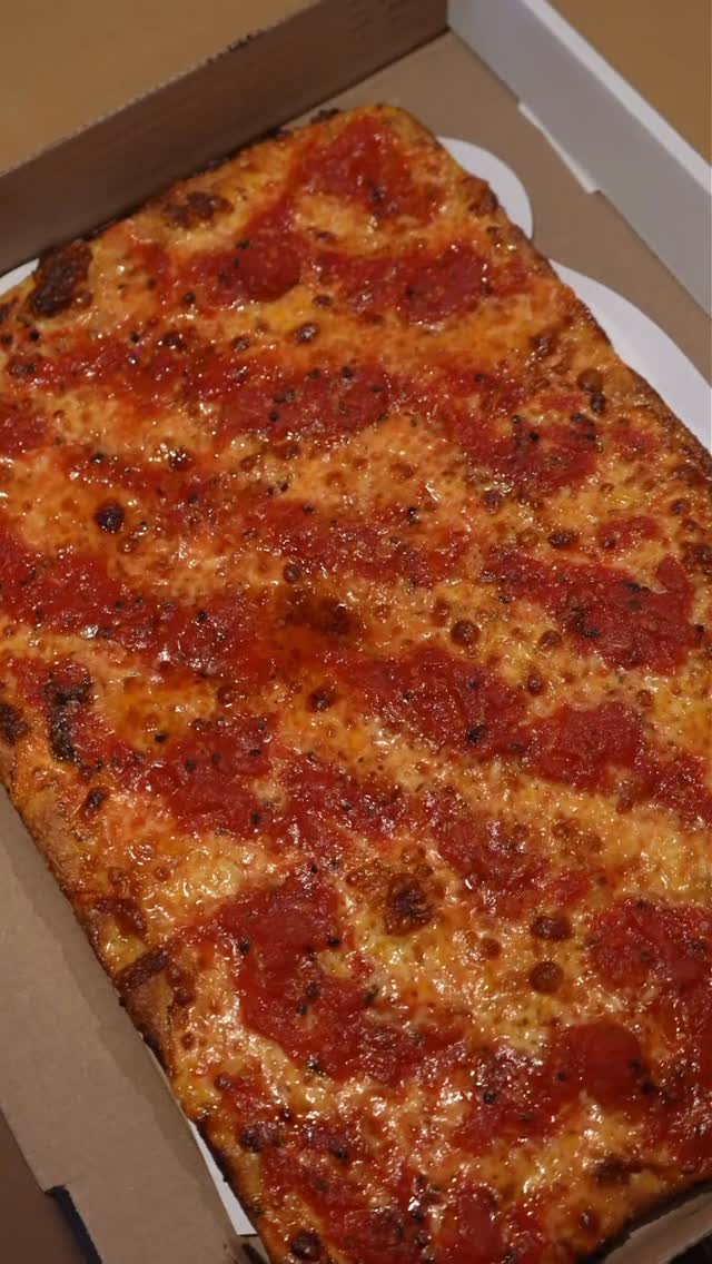 Square Grandma pie in an olive-oil pan — crisp golden bottom, fresh tomato strips, slow-baked garlic chunks, melted mozzarella, pecorino dusting on top.